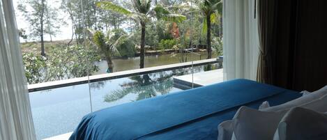 Un dormitorio con un ventanal que da a una piscina y follaje tropical.