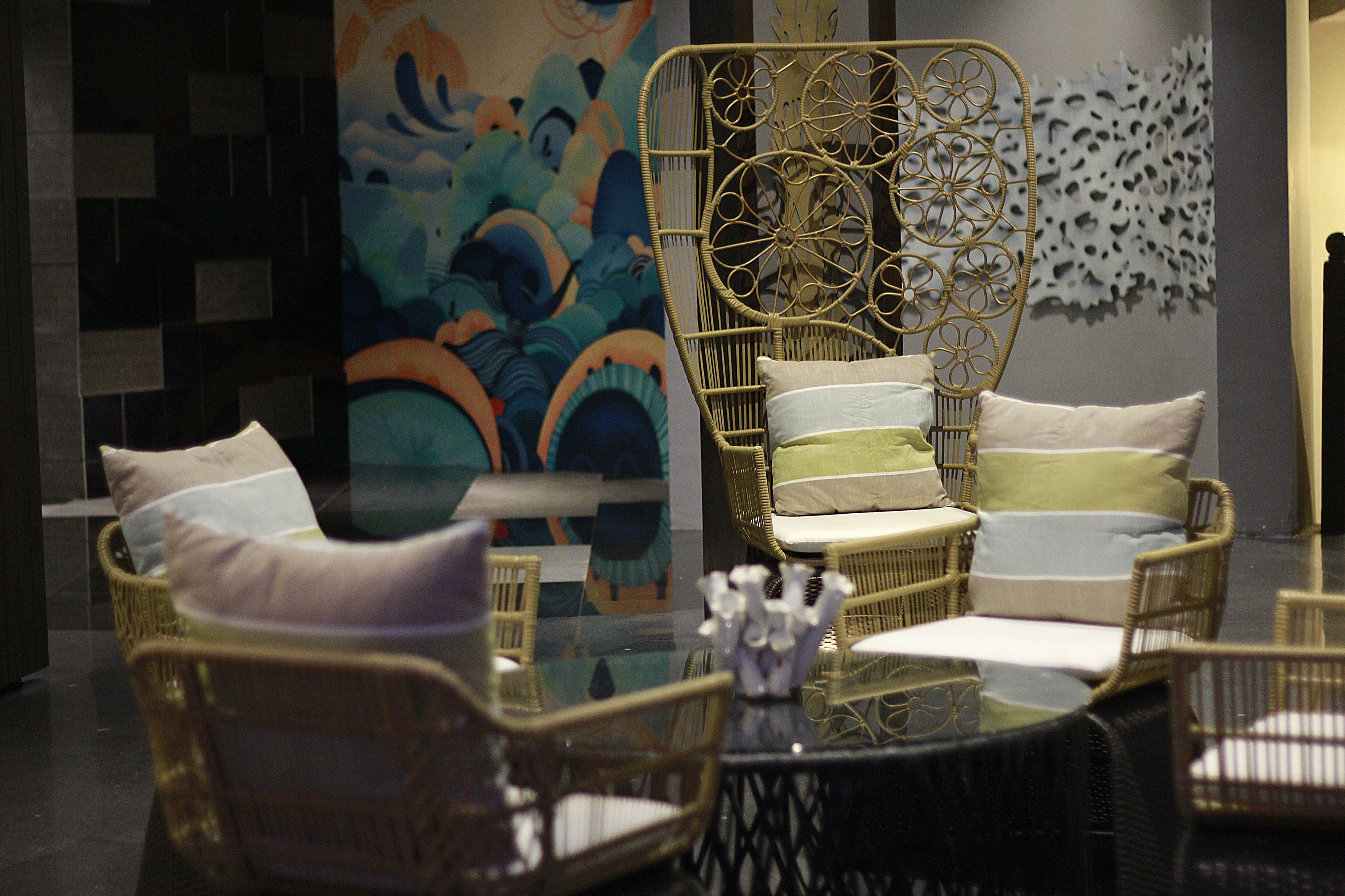 A room with wicker furniture, including a sofa and chairs, a glass coffee table, and a decorative wall piece.