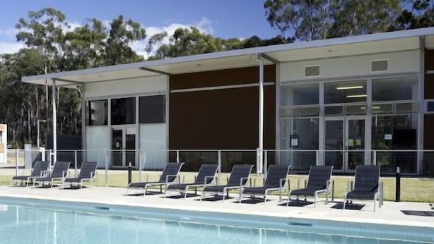 A modern building with a swimming pool, sun loungers, and a covered seating area. - Griffith University Village (Southport)