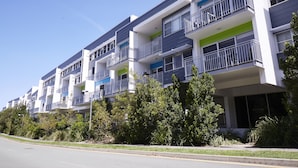 A modern multi-story residential building with balconies, large windows, and a well-maintained lawn. - Griffith University Village (Southport)