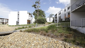 A modern residential building with a flat roof, multiple balconies, and a landscaped area with rocks and shrubs. - Griffith University Village (Southport)