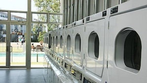 A row of white laundry machines in a spacious, well-lit room with large windows. - Griffith University Village (Southport)