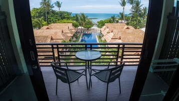 Balcón con mesa y sillas, vistas a una piscina y palmeras.