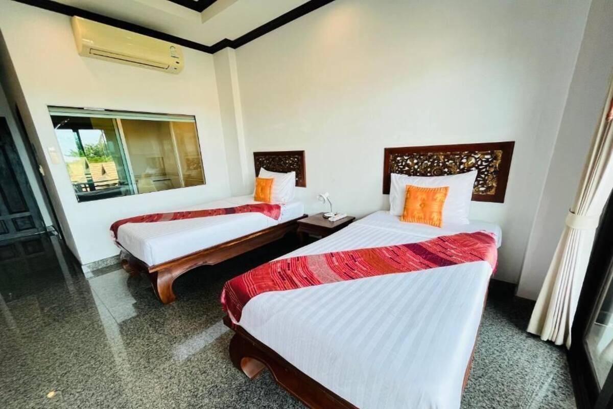 Habitación de hotel con dos camas individuales, cabecera de madera, mesita de noche y ventana con cortinas.