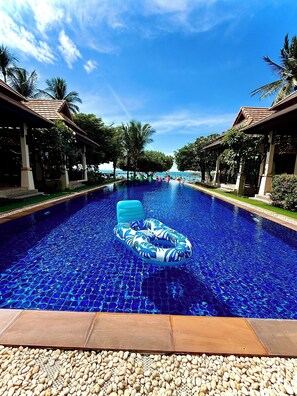 Piscina com um flutuador, cercada por palmeiras e passarelas cobertas.