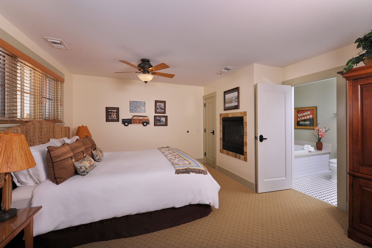 A bedroom with a bed, a ceiling fan, a fireplace, and a bathroom visible through an open door.