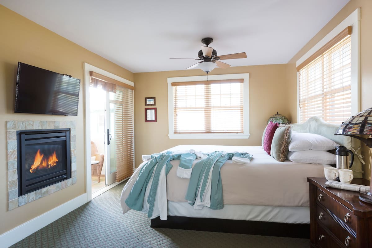 A bedroom with a fireplace, a bed, a ceiling fan, and a window with blinds.