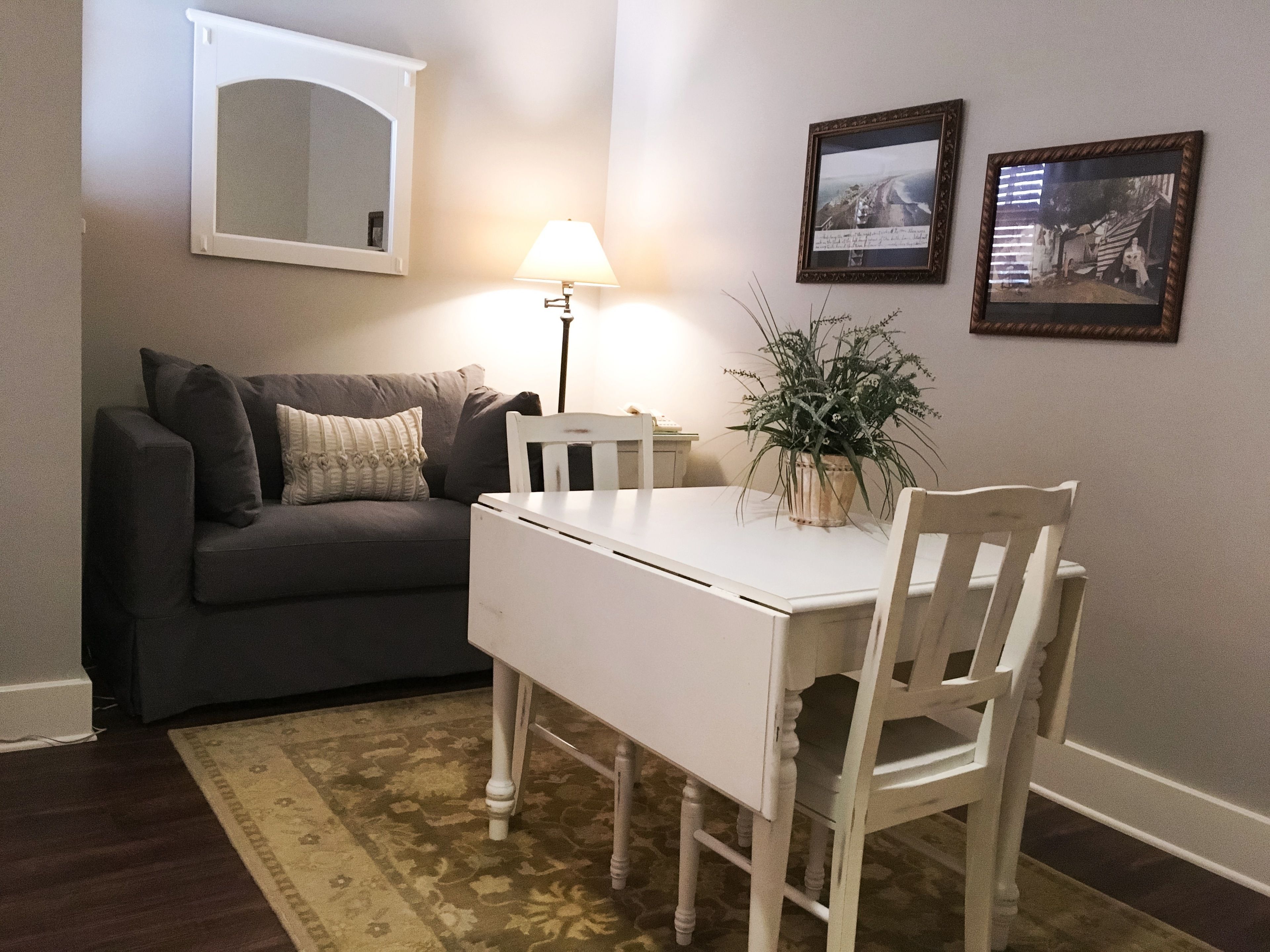 A living room with a dark grey sofa, a white table, a lamp, and two framed pictures on the wall.