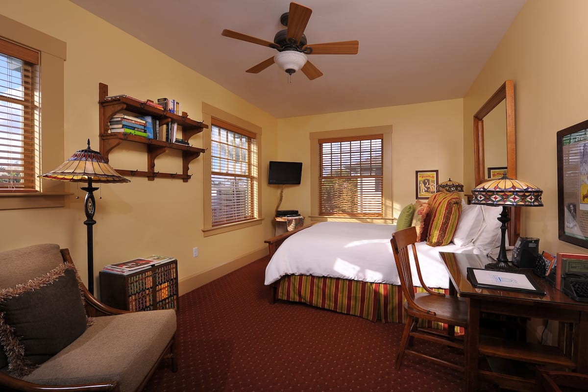 A bedroom with a bed, a desk, a chair, a ceiling fan, and a bookshelf.