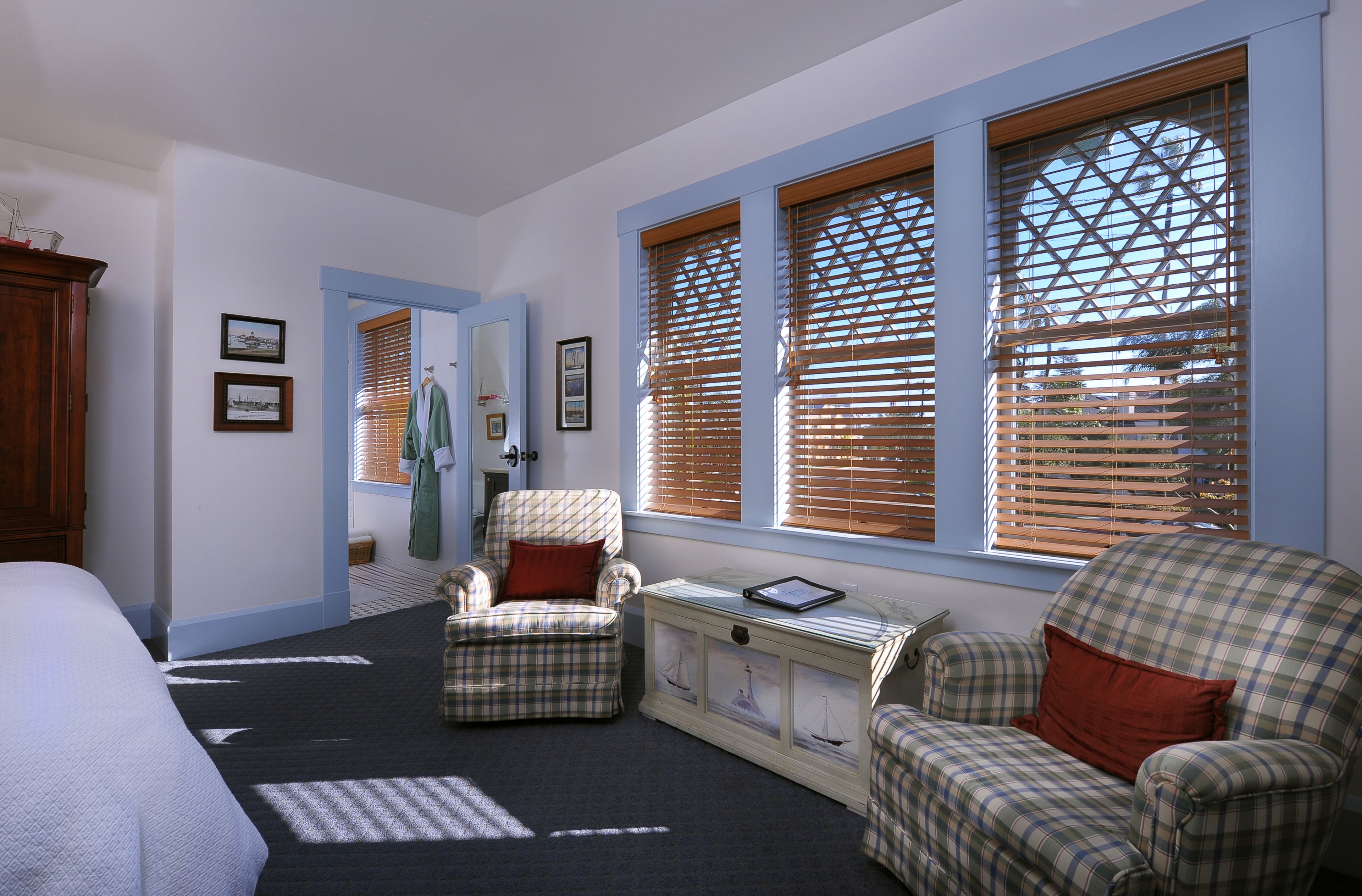 Une chambre à coucher avec un lit, deux fauteuils à motifs écossais, une commode et une fenêtre avec des stores.