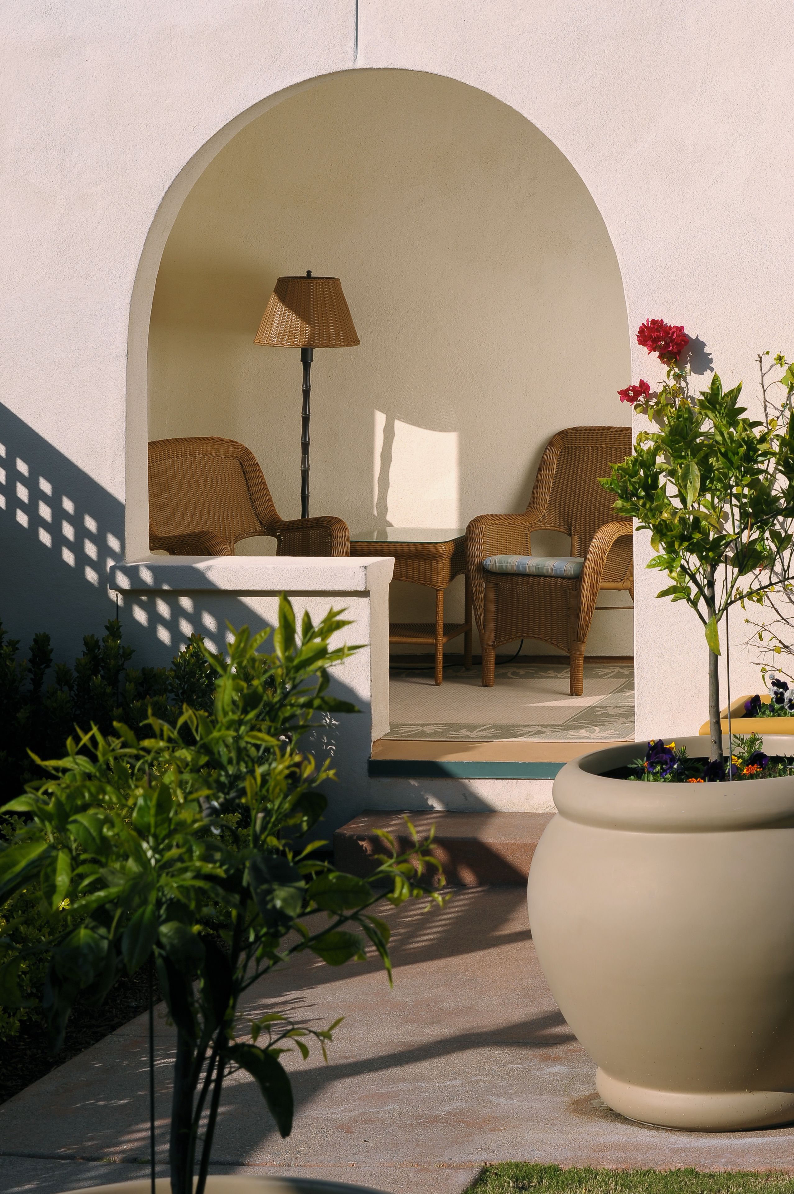 A patio with wicker furniture, a lamp, and a potted plant.