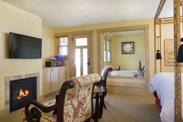 A hotel room with a fireplace, a television, a dining area with a chair, and a view of the bathroom. - 1906 Lodge (Coronado)