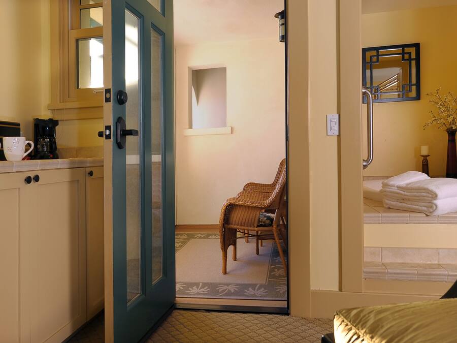 Quarto de hotel com cozinha compacta, uma cadeira, uma cama e banheiro com espelho e porta-toalhas.