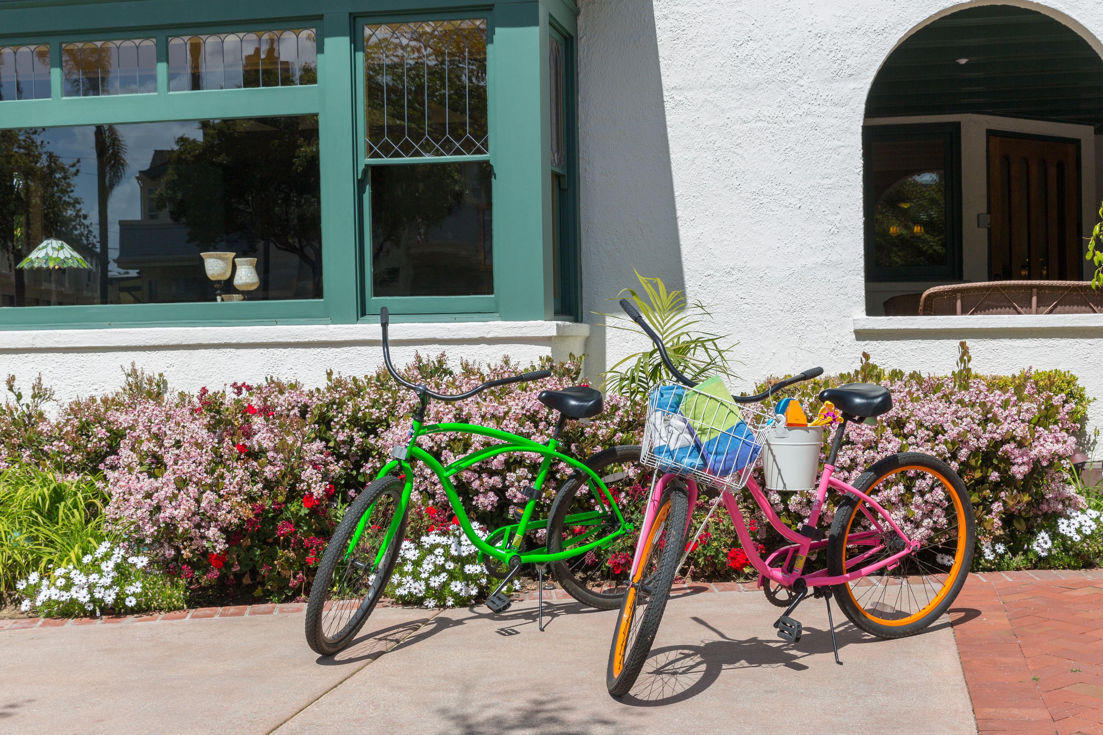 A green and pink bicycle parked in front of a building with a white exterior and green window frames.