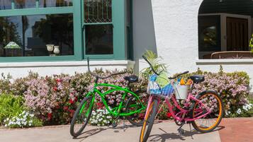 A green and pink bicycle parked in front of a building with a white exterior and green window frames.