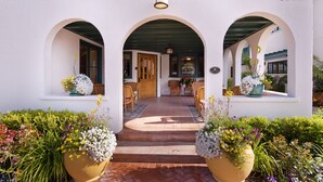 A hotel entrance with a covered patio, outdoor seating, and large flower planters. - 1906 Lodge (Coronado)