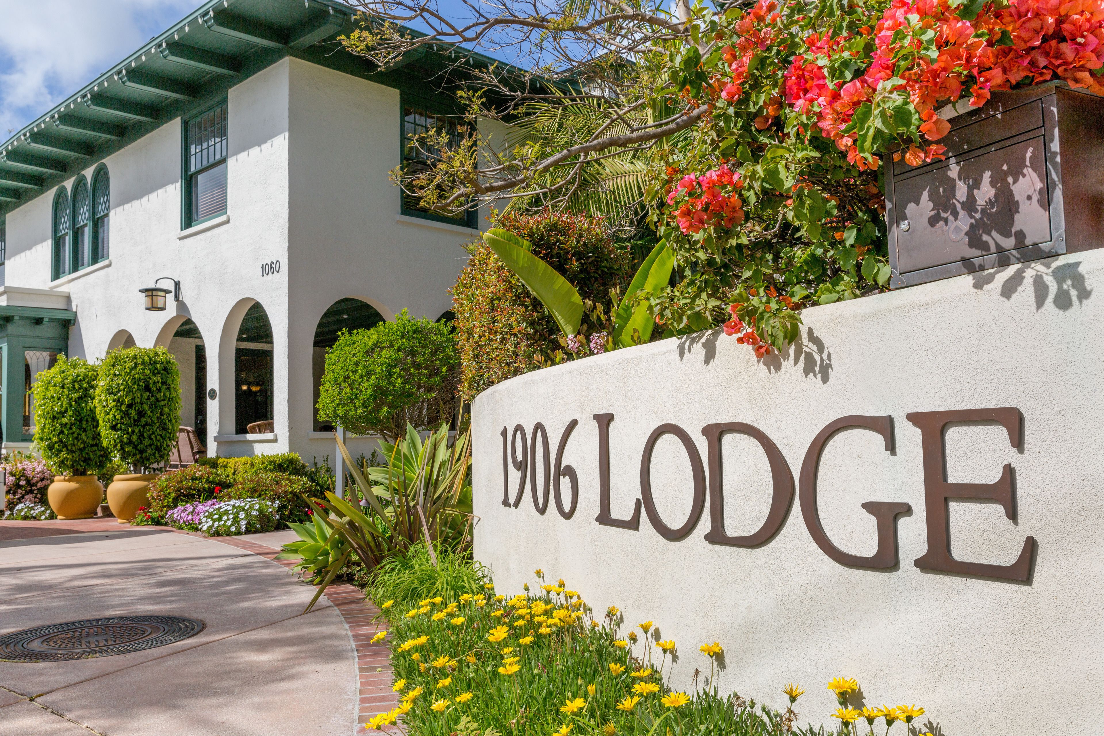 A building with the number 1906 on a sign, surrounded by lush greenery and flowers.