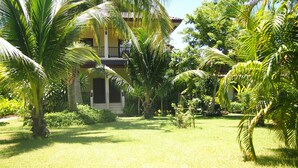 A lush garden with palm trees, a yellow building with a balcony, and a well-maintained lawn. - Manita Resort (Koh Samui)