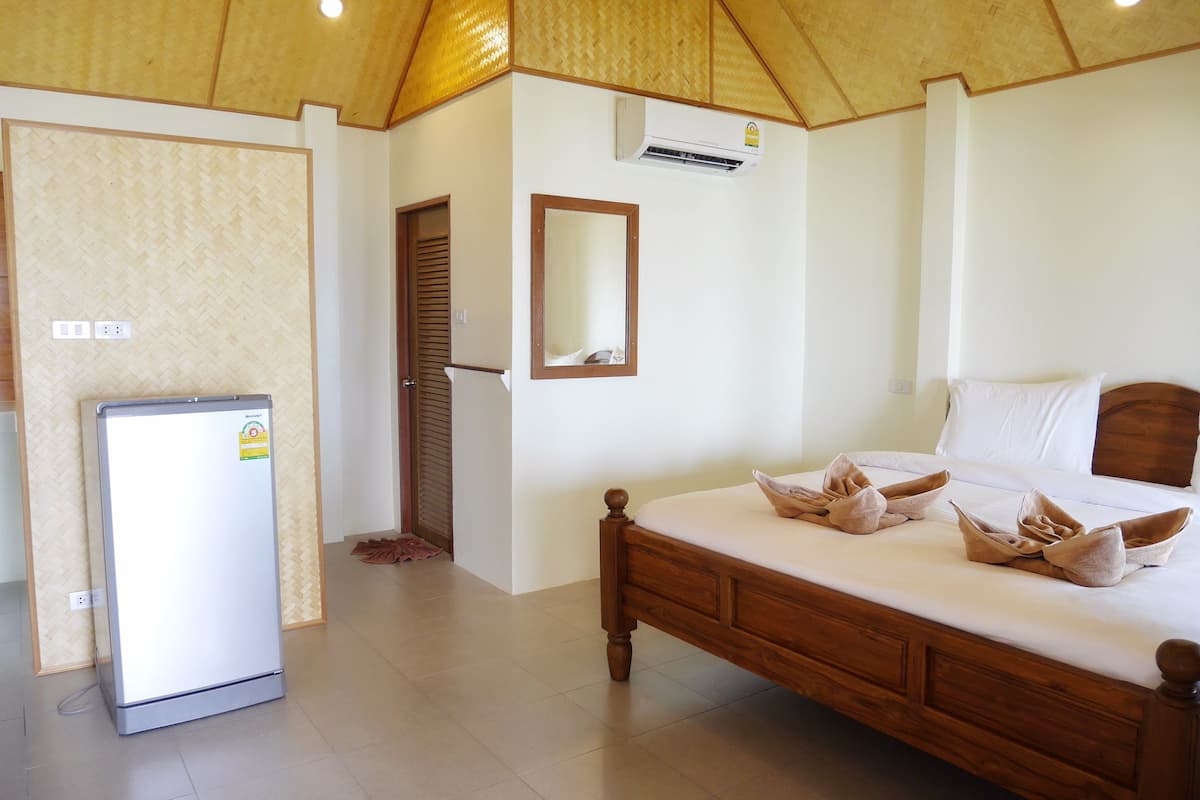 Un dormitorio con cama de madera, un refrigerador pequeño, un espejo y un equipo de aire acondicionado.