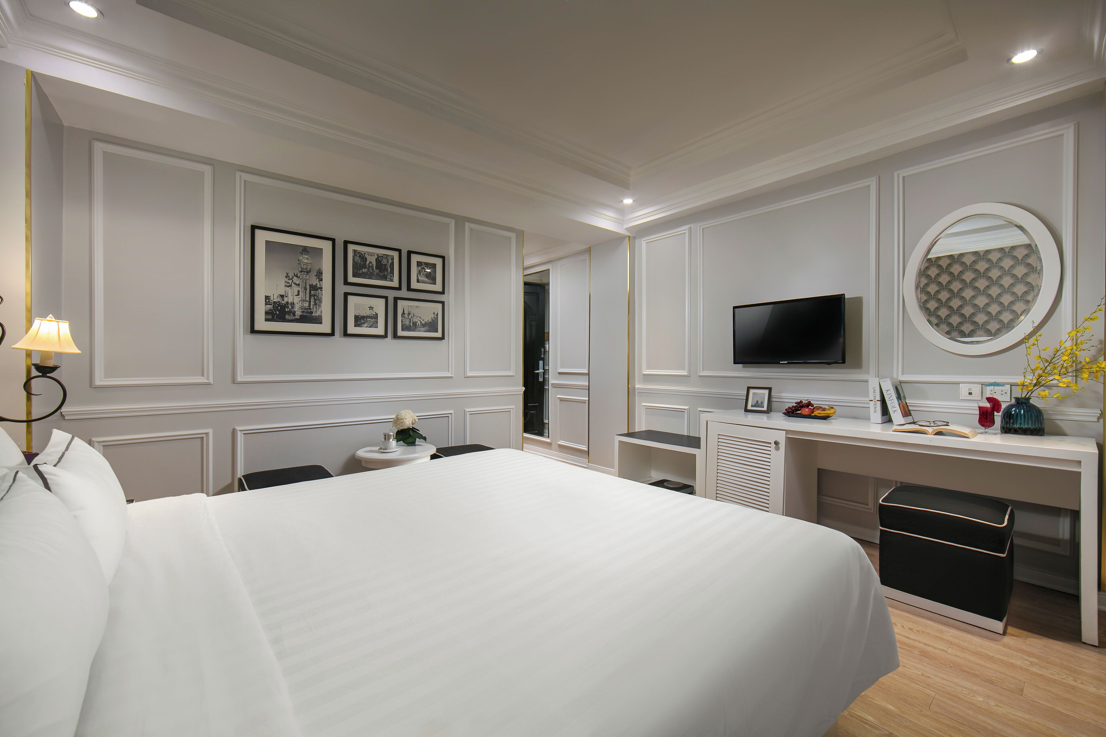 Quarto de hotel com uma cama grande, uma escrivaninha com televisão e quadros nas paredes.