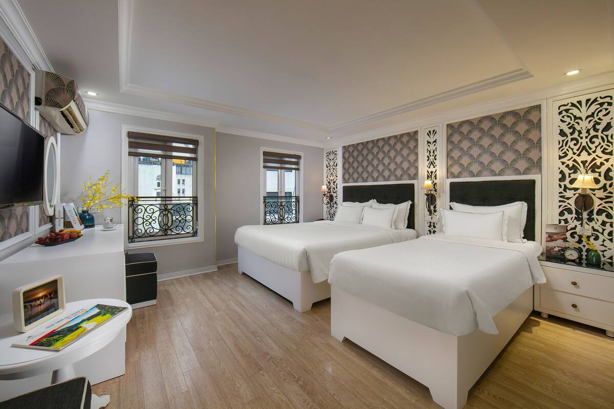 A hotel room with two beds, a TV, a balcony, and a desk with a chair.