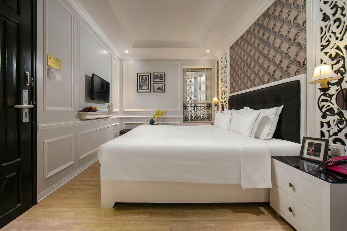 A hotel room with a large bed, bedside tables, a TV, and a decorative wall.