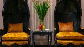 Two black wicker chairs with yellow cushions, a small table with a vase of flowers, and a bottle of water. - Lavender Central Hotel & Spa (Hanoi)