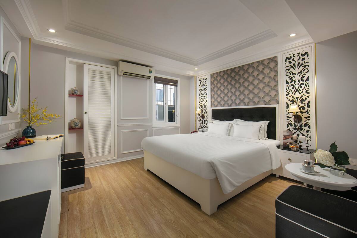 A modern bedroom with a large bed, a bedside table with a lamp, a dresser, and a window.