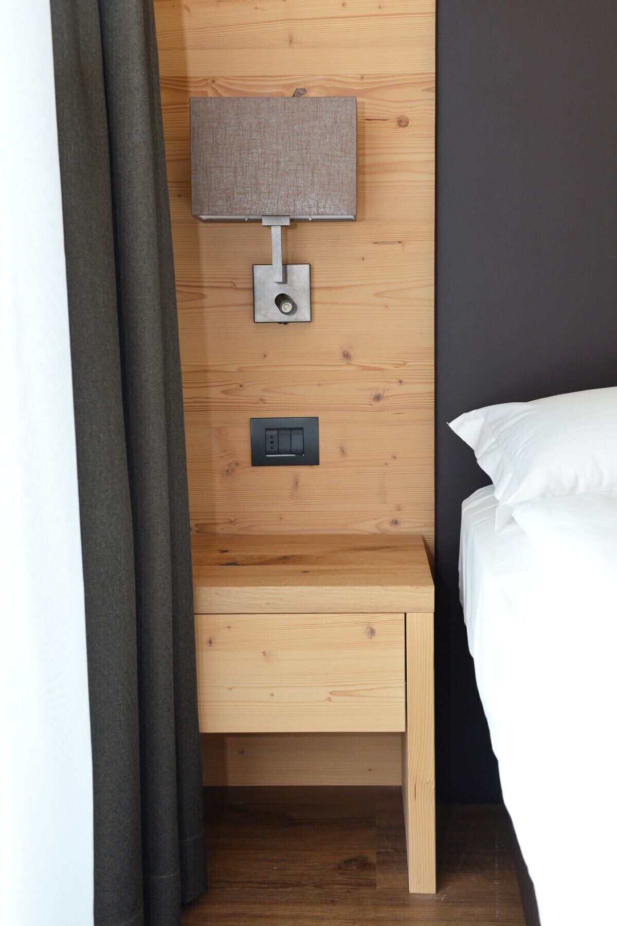 A wooden bedside table with a lamp and a power outlet.