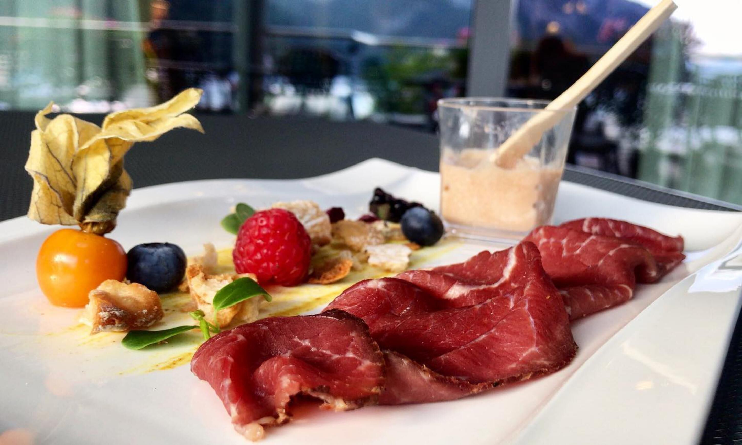 A plate with prosciutto, berries, and a glass of beverage.