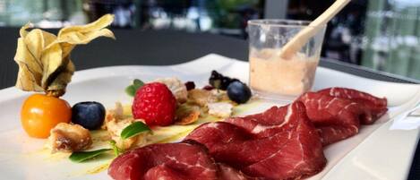 A plate with prosciutto, berries, and a glass of beverage.