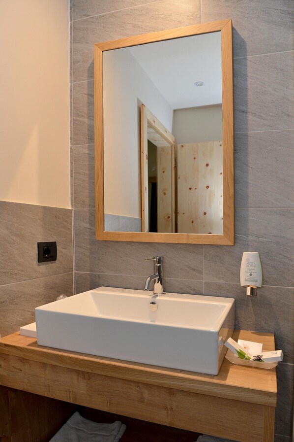 A bathroom with a white sink, a wooden-framed mirror, and a towel dispenser.
