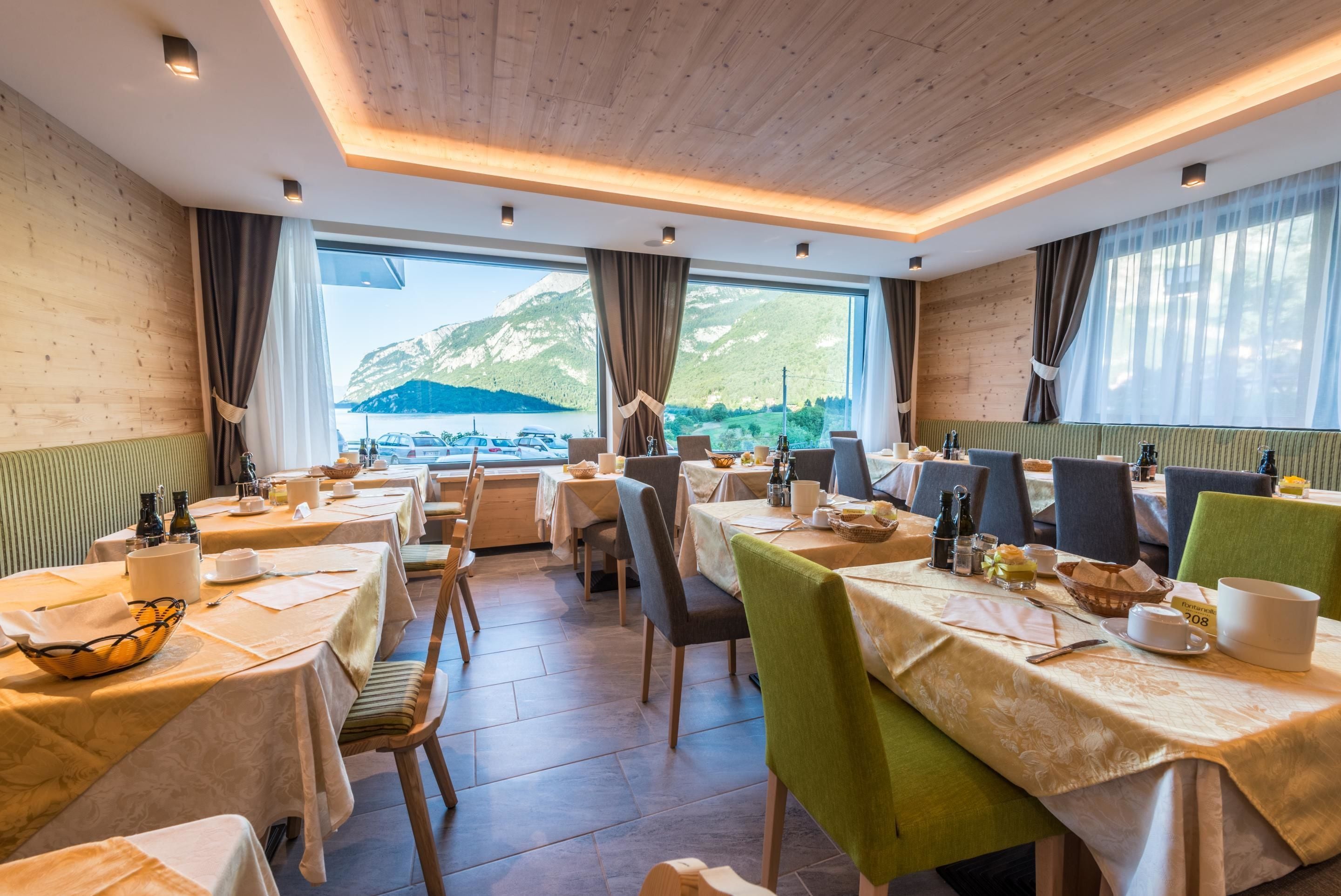 A restaurant with tables set for dining, large windows with mountain views, and a wooden ceiling.