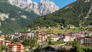 A mountain town with buildings surrounded by forested hills and rocky mountains. - Feeling Hotel Fontanella (Molveno)