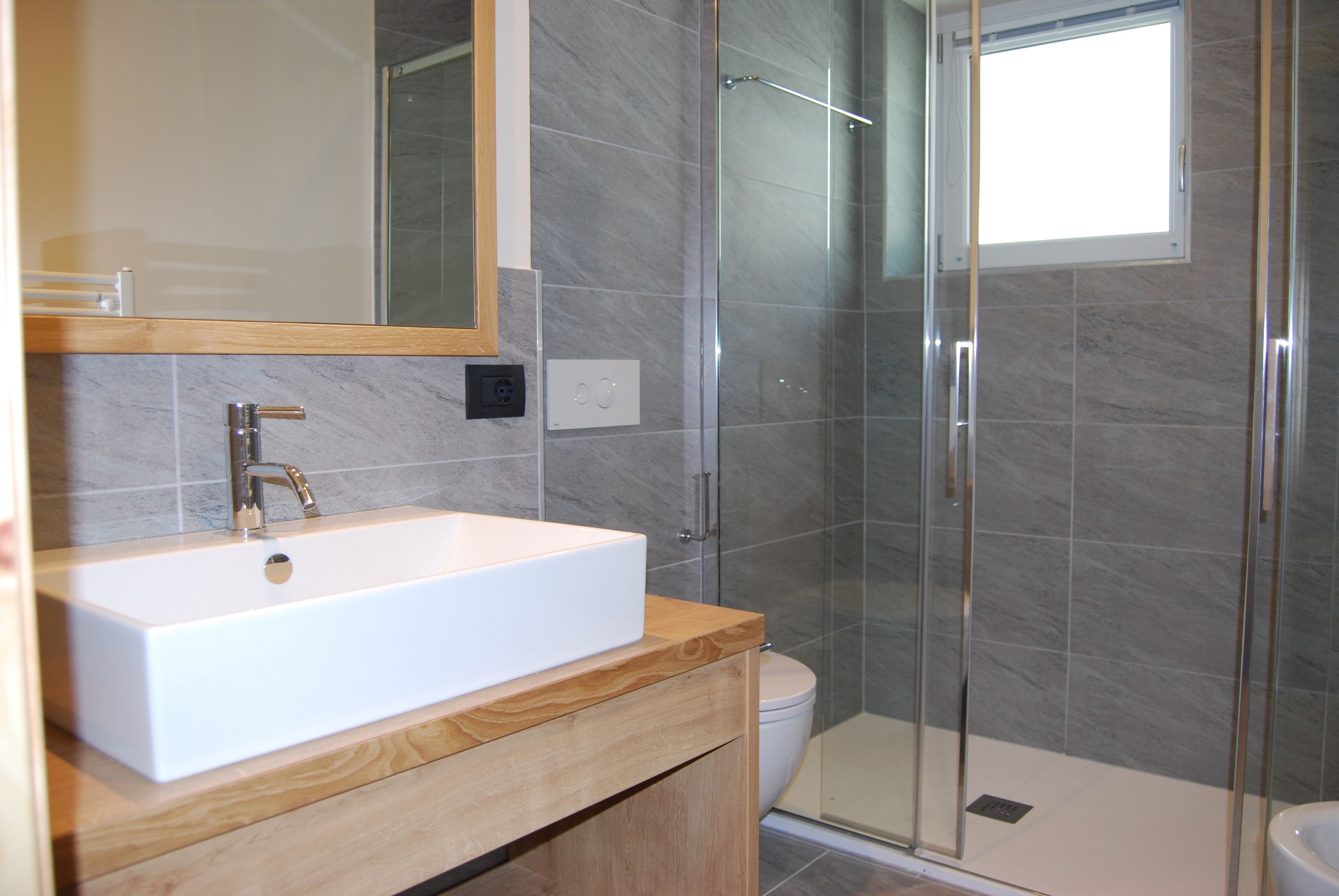 A modern bathroom with a rectangular sink, wooden vanity, glass shower enclosure, and a toilet.