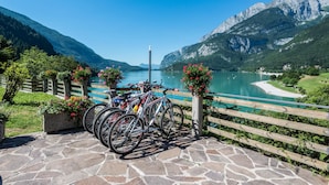 A stone-paved area with bicycles parked near a wooden fence overlooking a lake and mountains. - Feeling Hotel Fontanella (Molveno)