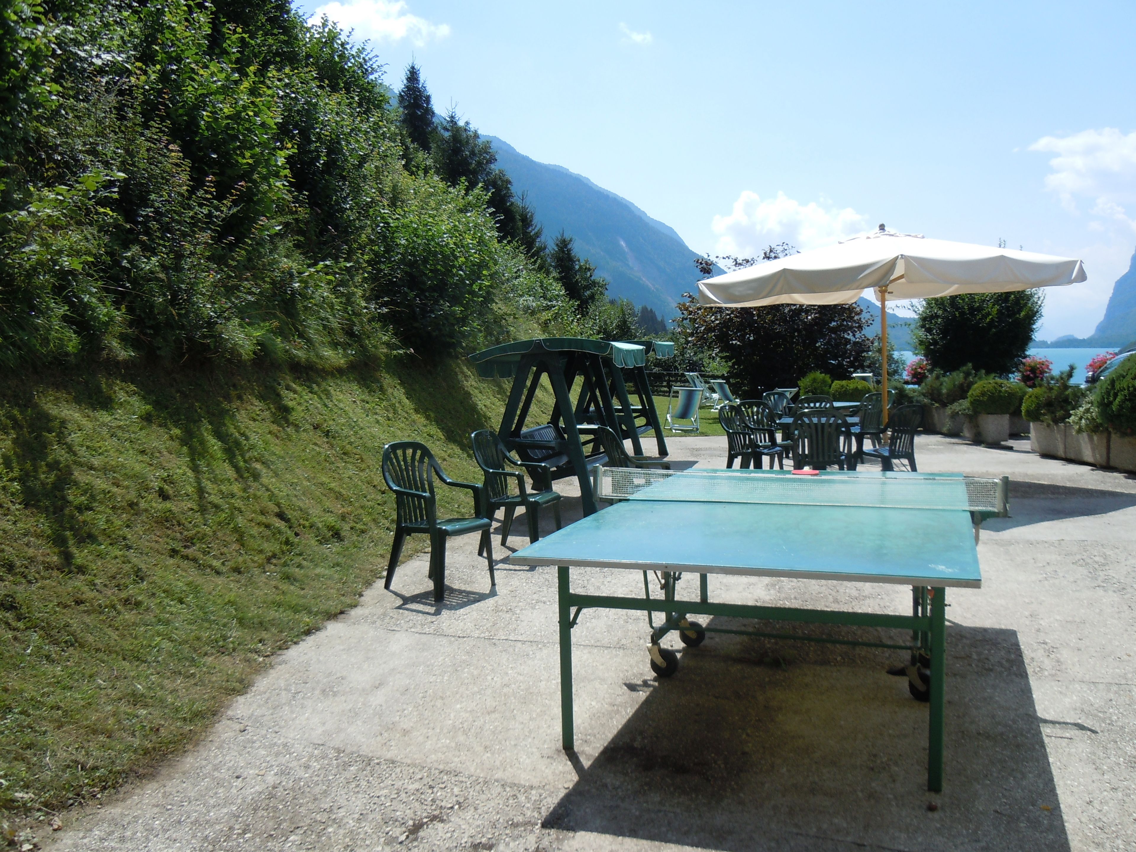 Een terras met tafels en stoelen, een tafeltennistafel en een witte parasol.