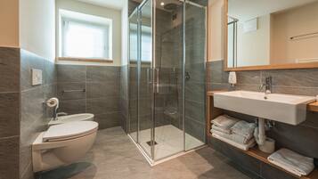 A modern bathroom with a glass-enclosed shower, a toilet, and a sink with towels.