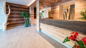 A reception area with wooden panel walls, a reception desk, and potted plants. - Feeling Hotel Fontanella (Molveno)