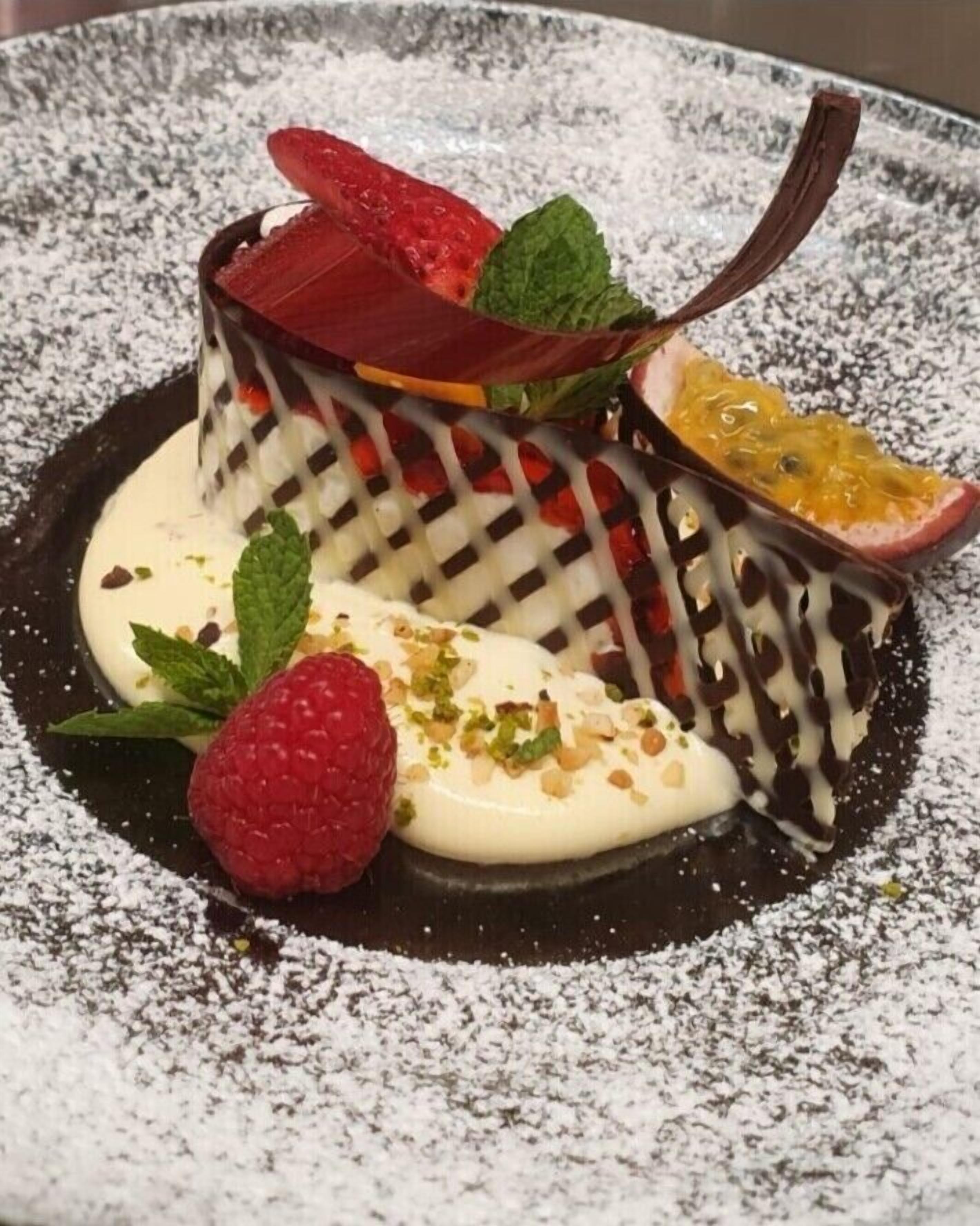 Un postre con fresas, menta y chocolate sobre un plato espolvoreado con azúcar glas.