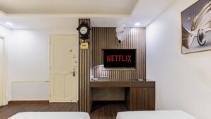 Une chambre d’hôtel avec un bureau en bois, une télévision, une horloge et une porte portant un numéro.