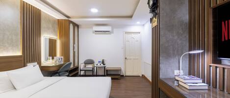 Habitación de hotel con una cama, un escritorio con lámpara, una silla, una mesita con tetera y un televisor.