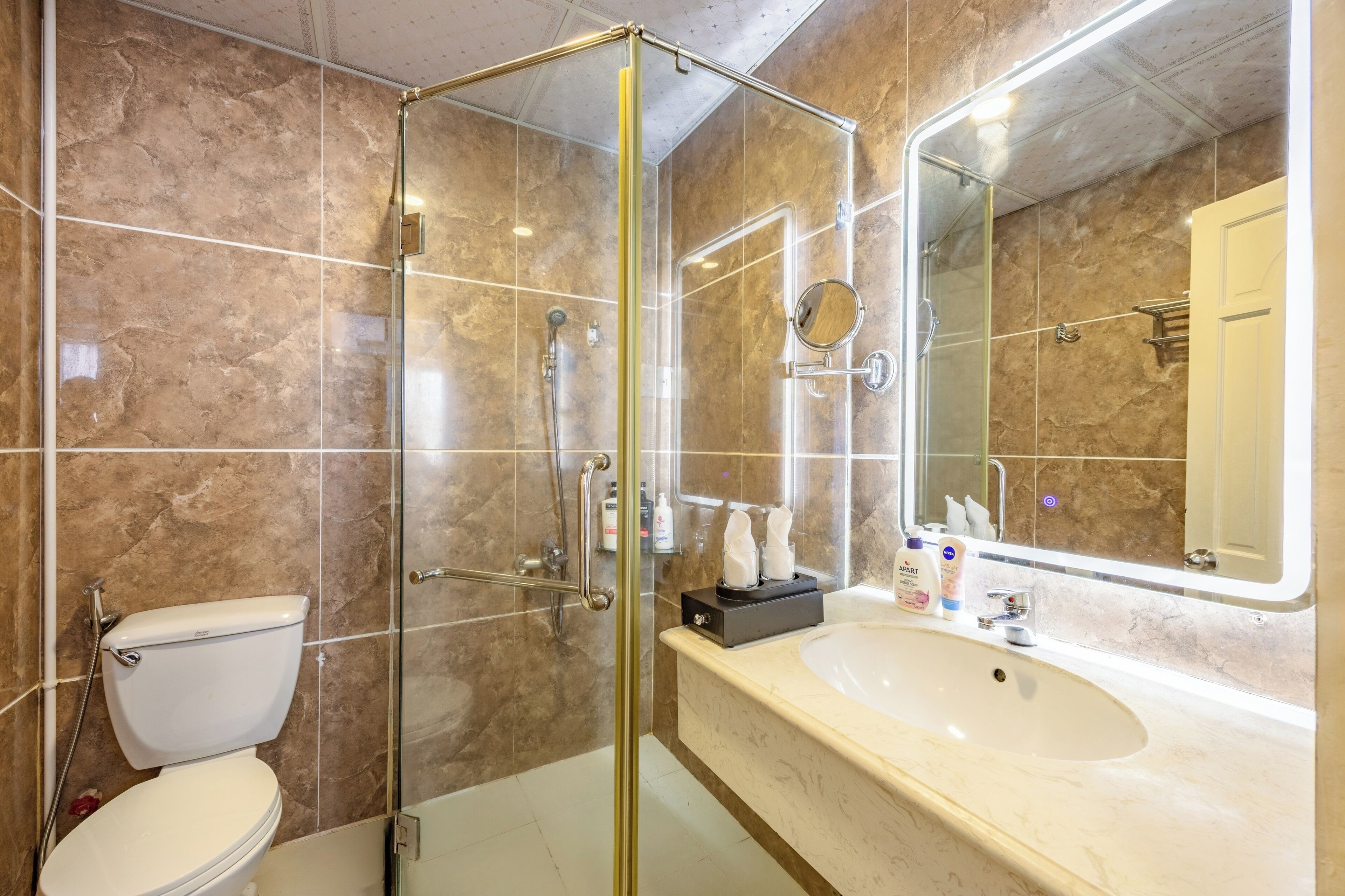 A modern bathroom with a glass-enclosed shower, a white toilet, and a large sink with a mirror.