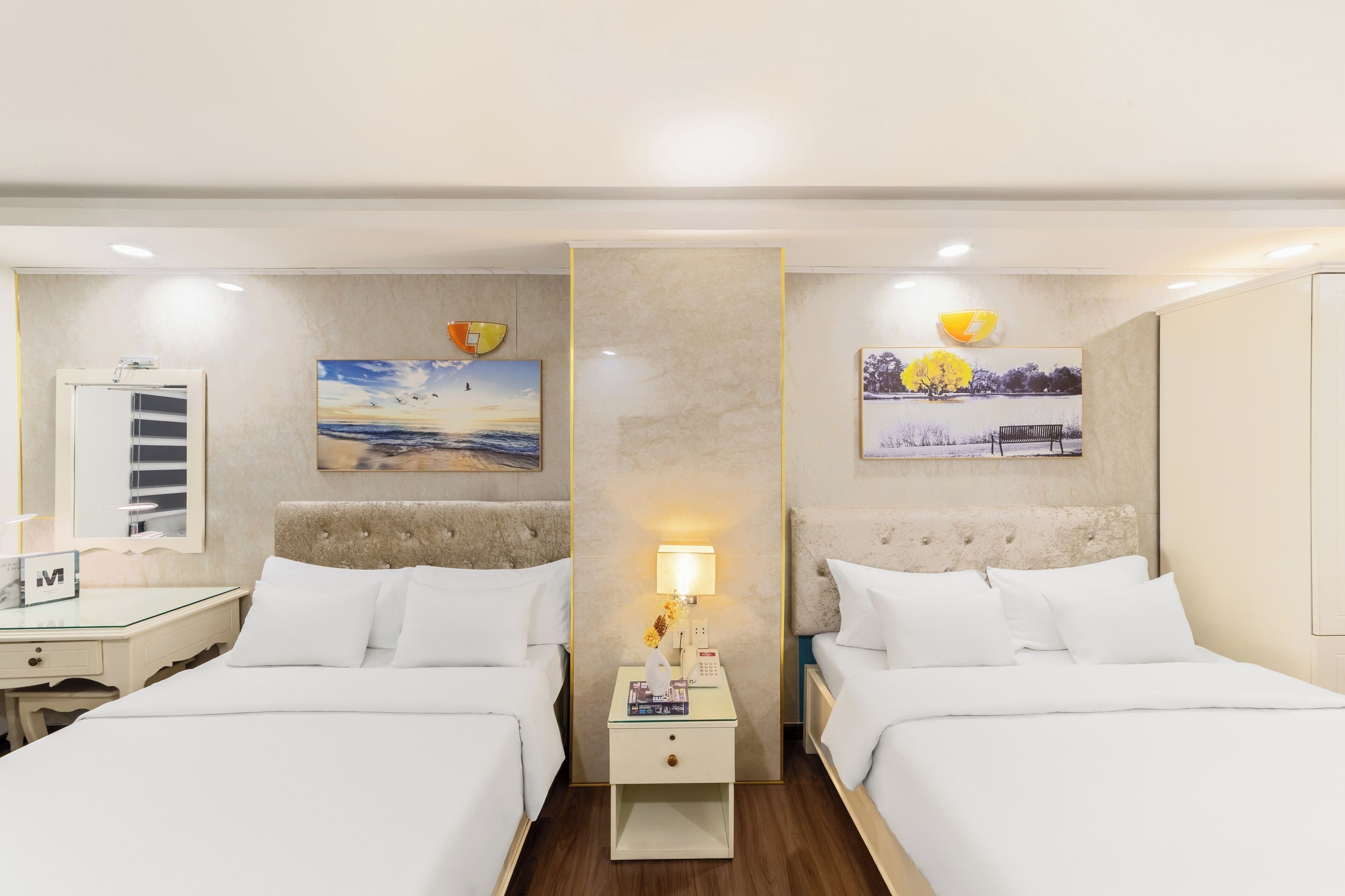 A hotel room with two beds, a nightstand with a lamp, a mirror, and artwork on the walls.