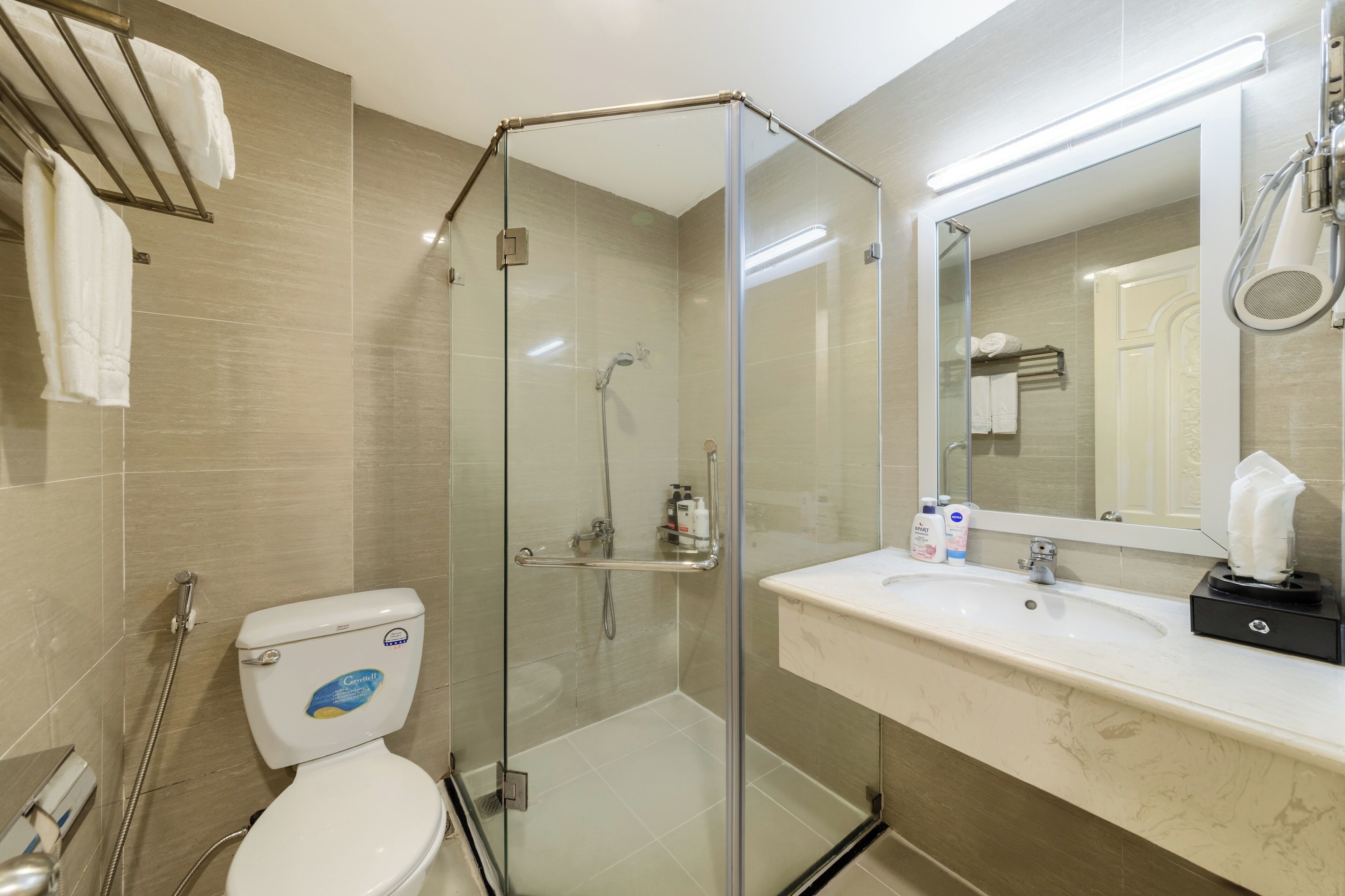 A modern bathroom with a glass-enclosed shower, a white toilet, a marble sink, and a large mirror.