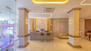 Un hall d’hôtel moderne avec un comptoir d’accueil, deux tabourets de bar, un canapé et une horloge murale.