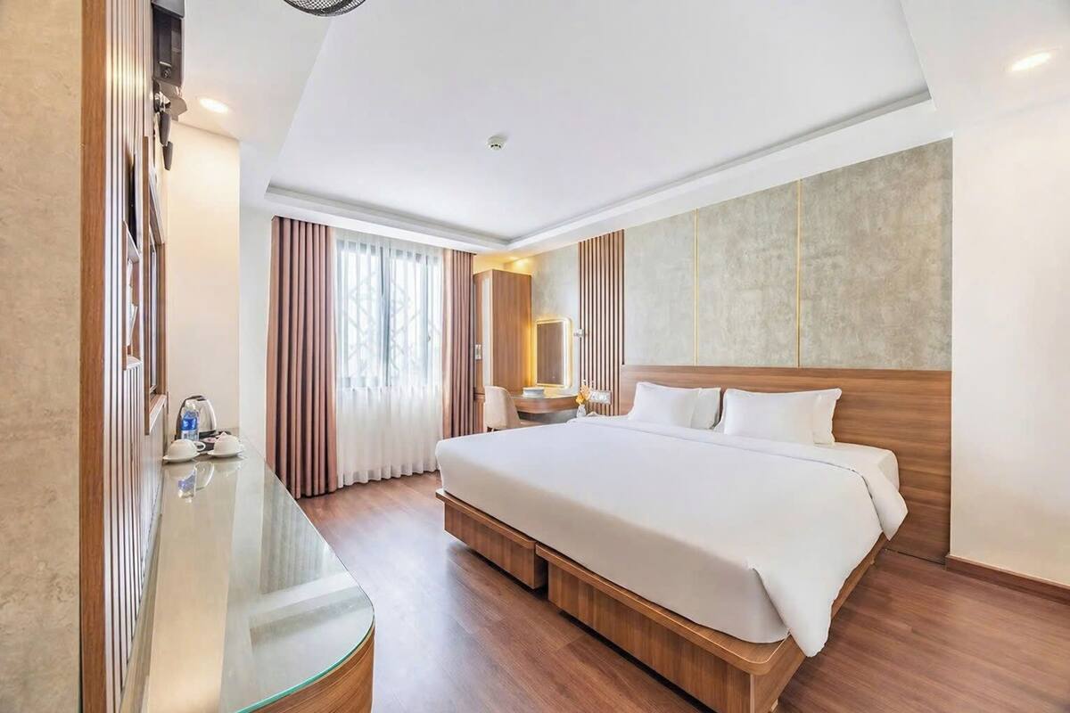 Ein Hotelzimmer mit einem großen Bett, einem Glastisch, einem Spiegel und einem Fenster mit Vorhängen.