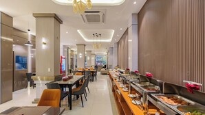 Un espace de restauration moderne dans un hôtel, avec un buffet, des tables et des chaises disposées de manière agréable, et un éclairage contemporain.