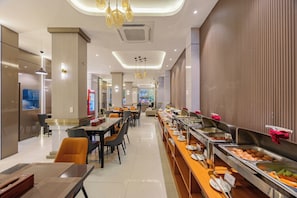 Un espace de restauration moderne dans un hÎtel, avec un buffet, des tables et des chaises disposées de maniÚre agréable, et un éclairage contemporain.