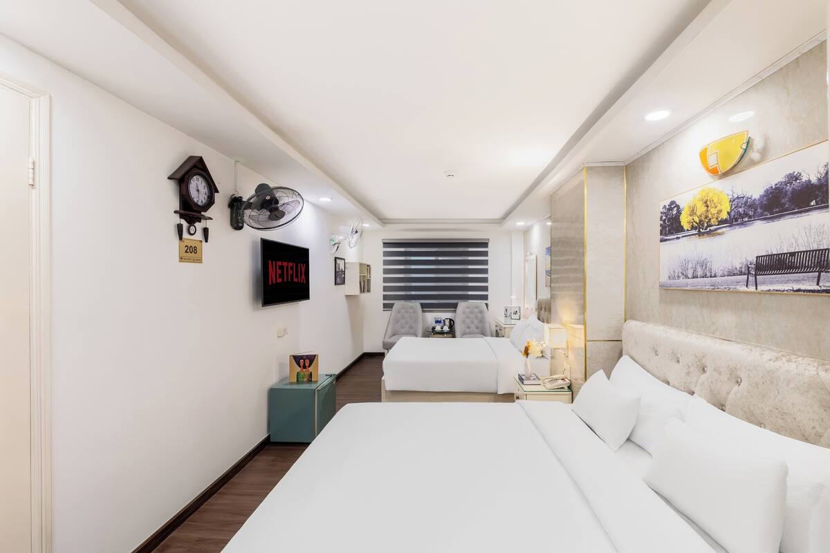 Ein Hotelzimmer mit einem großen Bett, einem kleineren Bett, einem Fernseher, einer Uhr und einem Bild an der Wand.